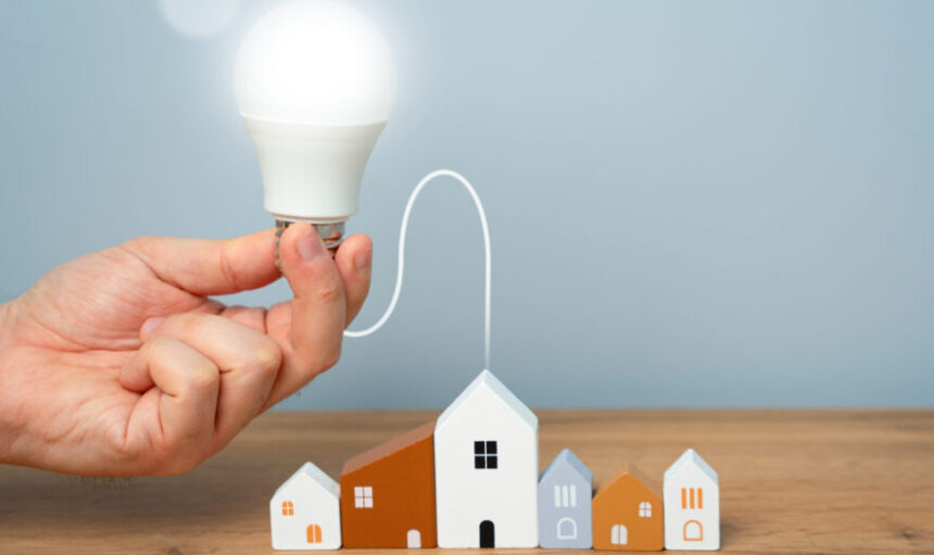 Hand connects light bulb to residential buildings. Concept of power supply. Innovations and technologies of smart home. Autonomous energy and housing. Energy saving.